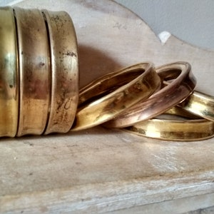 May include: A set of five brass napkin rings, stacked and arranged in a casual manner. The rings are polished and have a warm, golden hue.