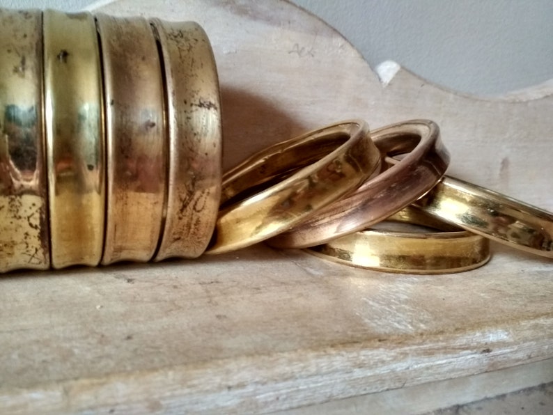 May include: A set of five brass napkin rings, stacked and arranged in a casual manner. The rings are polished and have a warm, golden hue.