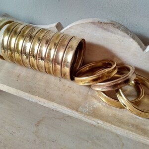 May include: A stack of 12 brass rings, some are stacked on top of each other, while others are spread out on a light wood surface.