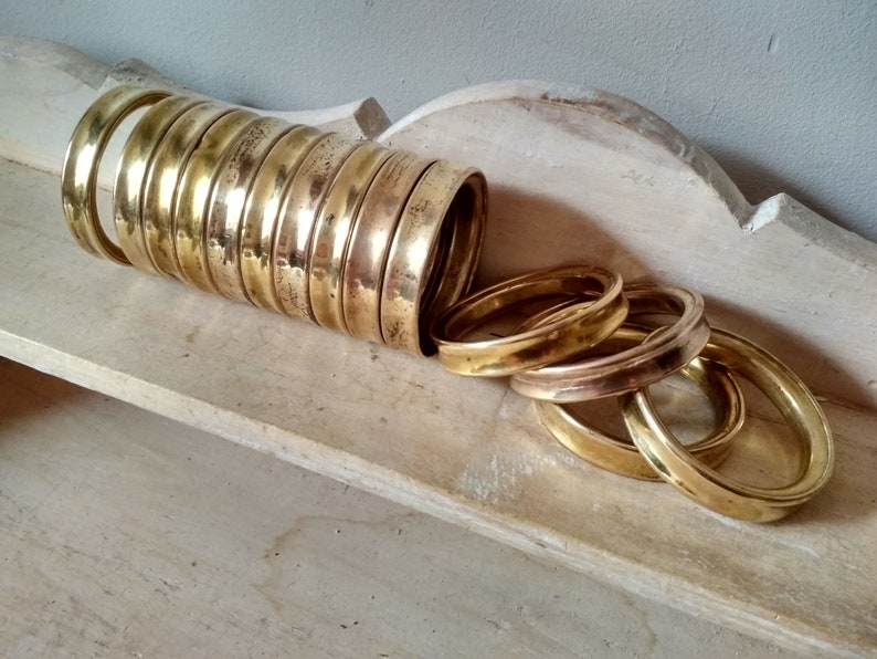 May include: A stack of 12 brass rings, some are stacked on top of each other, while others are spread out on a light wood surface.