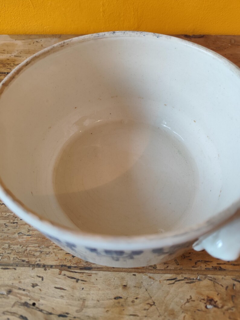 K&ouml;nnte beinhalten: Wei&szlig;e Keramiksch&uuml;ssel mit einem blauen und wei&szlig;en Blumenmuster. Die Sch&uuml;ssel hat einen einzigen Henkel und ist am Rand leicht abgebrochen.