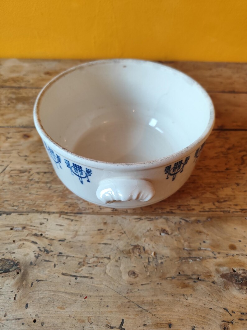 K&ouml;nnte beinhalten: Eine wei&szlig;e Keramiksch&uuml;ssel mit einem blauen und wei&szlig;en Blumenmuster. Die Sch&uuml;ssel hat einen einzigen Griff und ist perfekt zum Servieren von Suppe oder anderen Gerichten.
