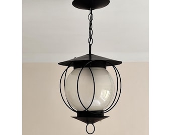 Lampada a sospensione anticata con globo in vetro opalino bianco e struttura in ferro battuto nero.