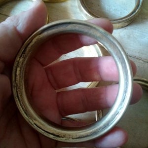 May include: A set of six gold-toned metal rings, each with a smooth, rounded edge. The rings are stacked on top of each other, with one ring being held in a hand.