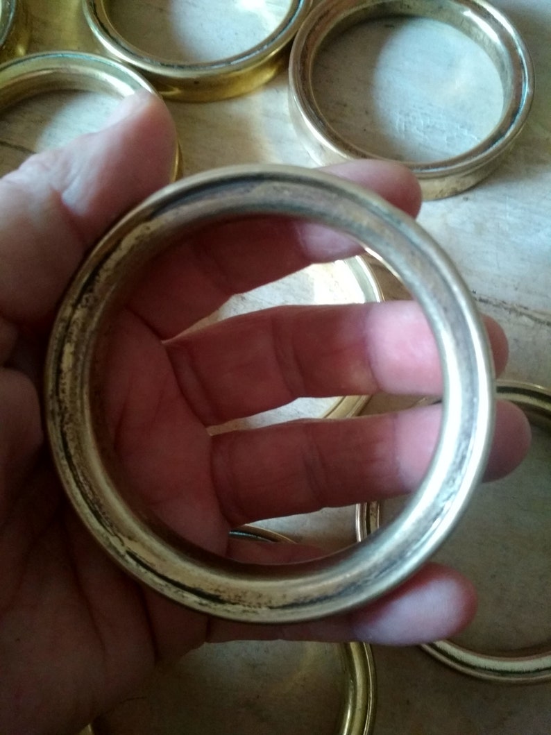 May include: A set of six gold-toned metal rings, each with a smooth, rounded edge. The rings are stacked on top of each other, with one ring being held in a hand.