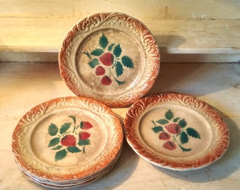 May include: A stack of eight vintage ceramic plates with a brown rim and a cream-colored center. Each plate features a hand-painted design of red strawberries with green leaves.