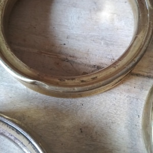 May include: Two gold-colored metal rings, possibly for a curtain rod or other decorative purpose, are lying on a wooden surface.