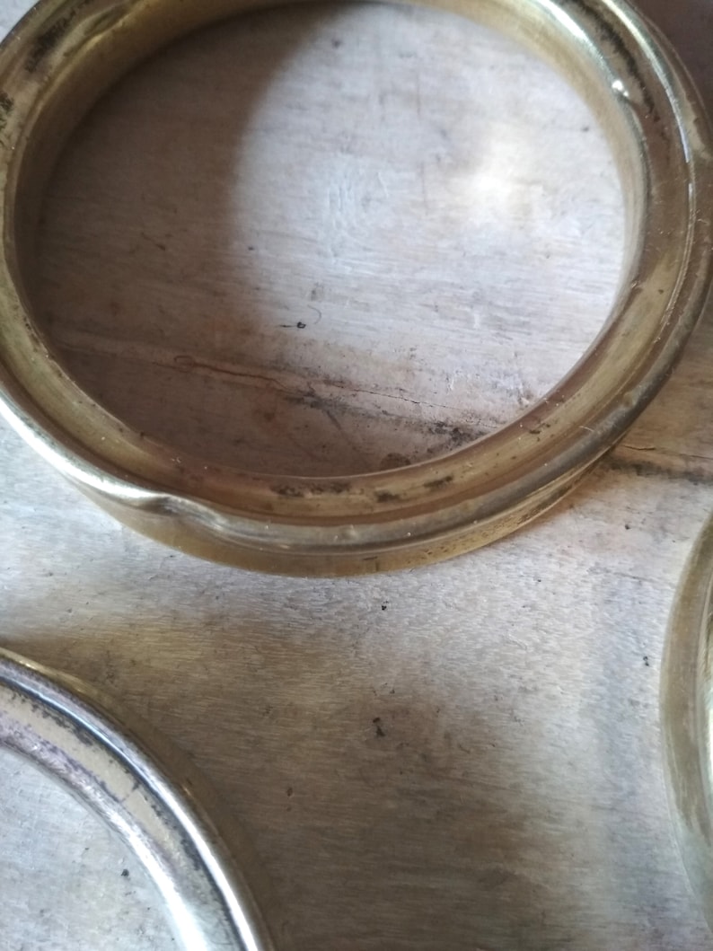 May include: Two gold-colored metal rings, possibly for a curtain rod or other decorative purpose, are lying on a wooden surface.