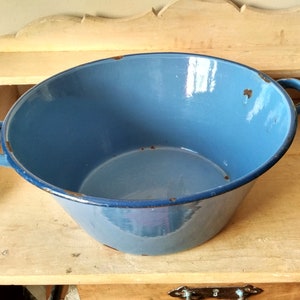 Op de afbeelding: Een grote, lichtblauwe emaille kom met twee handvatten. De kom heeft een versleten, vintage uitstraling met wat roestvlekken.