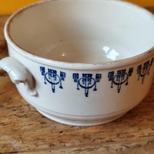 K&ouml;nnte beinhalten: Eine wei&szlig;e Keramiksch&uuml;ssel mit zwei Griffen und einem blauen und wei&szlig;en geometrischen Muster am Rand.