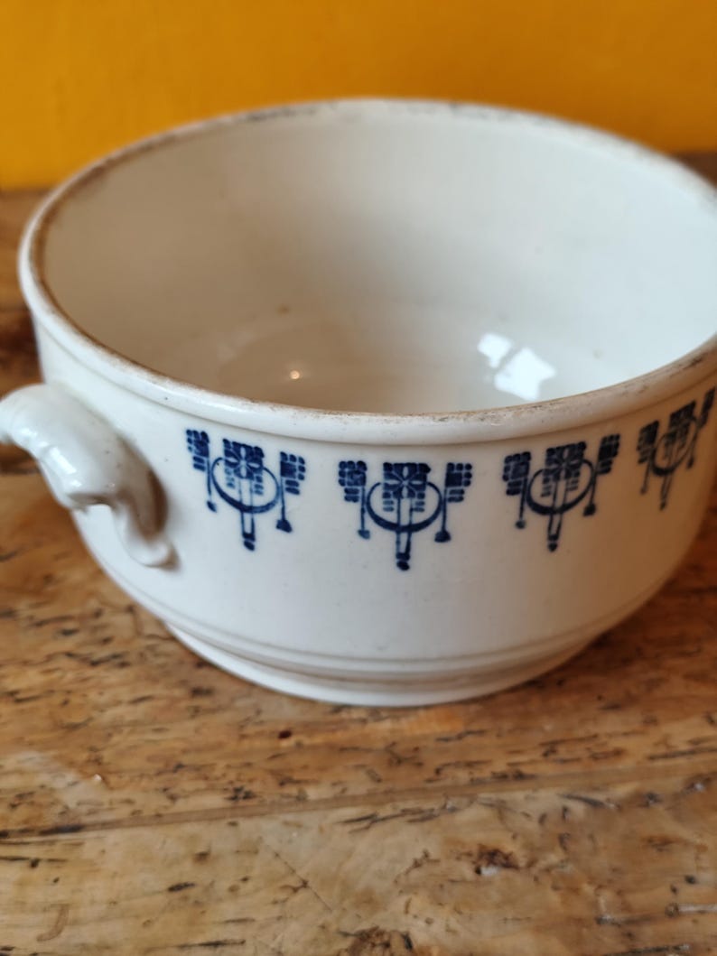 K&ouml;nnte beinhalten: Eine wei&szlig;e Keramiksch&uuml;ssel mit zwei Griffen und einem blauen und wei&szlig;en geometrischen Muster am Rand.