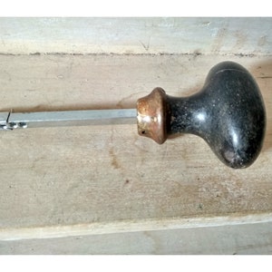 Peut inclure: Une poignée de porte noire et en laiton avec un long axe métallique fin. La poignée est de forme ovale et a une surface texturée.