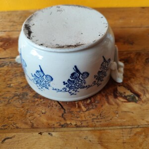 Op de afbeelding: Witte keramische pot met een blauw bloemenontwerp en twee handvatten. De pot staat op een houten oppervlak.