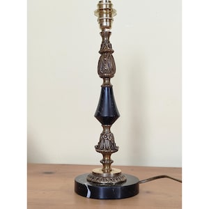 Peut inclure: Lampe de table vintage avec finition noire et dorée. La lampe présente une base ronde en marbre noir, un centre conique noir et des accents dorés ornés. La lampe mesure environ 46 cm de haut.