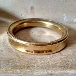 May include: A gold-colored metal ring with a rounded, slightly raised edge. The ring is smooth and shiny.