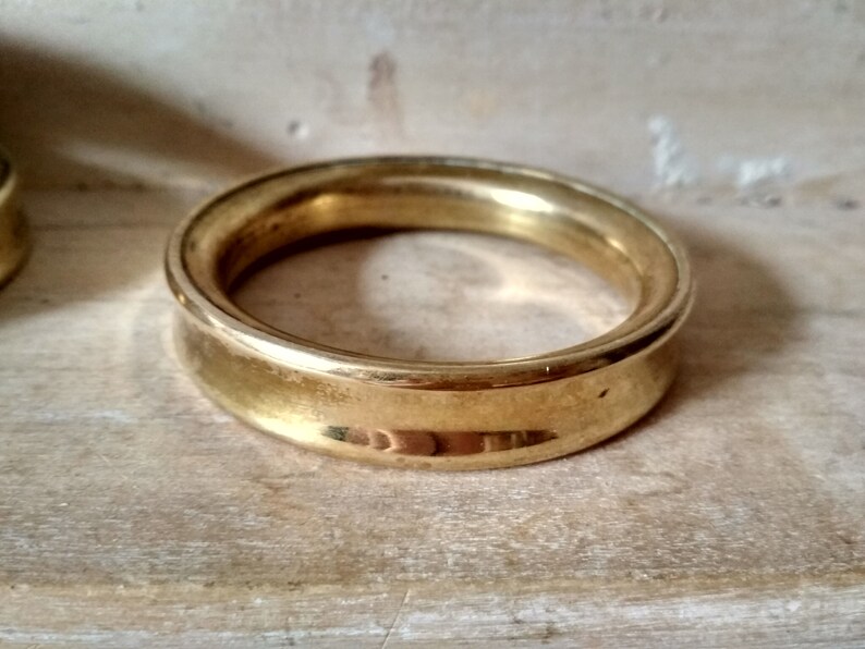 May include: A gold-colored metal ring with a rounded, slightly raised edge. The ring is smooth and shiny.