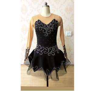 Puede incluir: Vestido negro de patinaje art&iacute;stico con mangas largas color nude y falda negra. El corpi&ntilde;o est&aacute; adornado con pedrer&iacute;a blanca. La falda tiene un dobladillo con volantes y una enagua negra transparente.