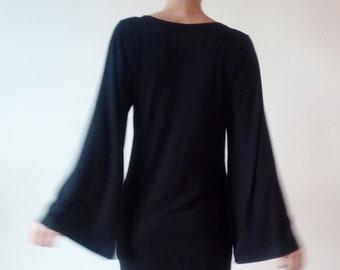 Peut inclure: Une robe noire à manches longues et larges et un corsage ajusté. La robe est associée à des collants noirs et des bottes à talons noirs.