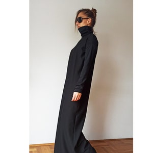 May include: A long, black turtleneck dress with long sleeves. The dress is floor-length and worn with black shoes. The person in the image is wearing sunglasses and has their hair up. The dress appears to be made of a soft, flowing fabric.