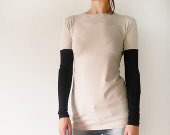 May include: A woman is wearing a beige long-sleeved shirt with black sleeves and blue jeans. She is wearing beige heeled sandals.