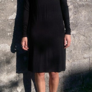 May include: A black turtleneck dress with long sleeves. The dress is fitted and falls to the knees. The model is wearing black shoes.