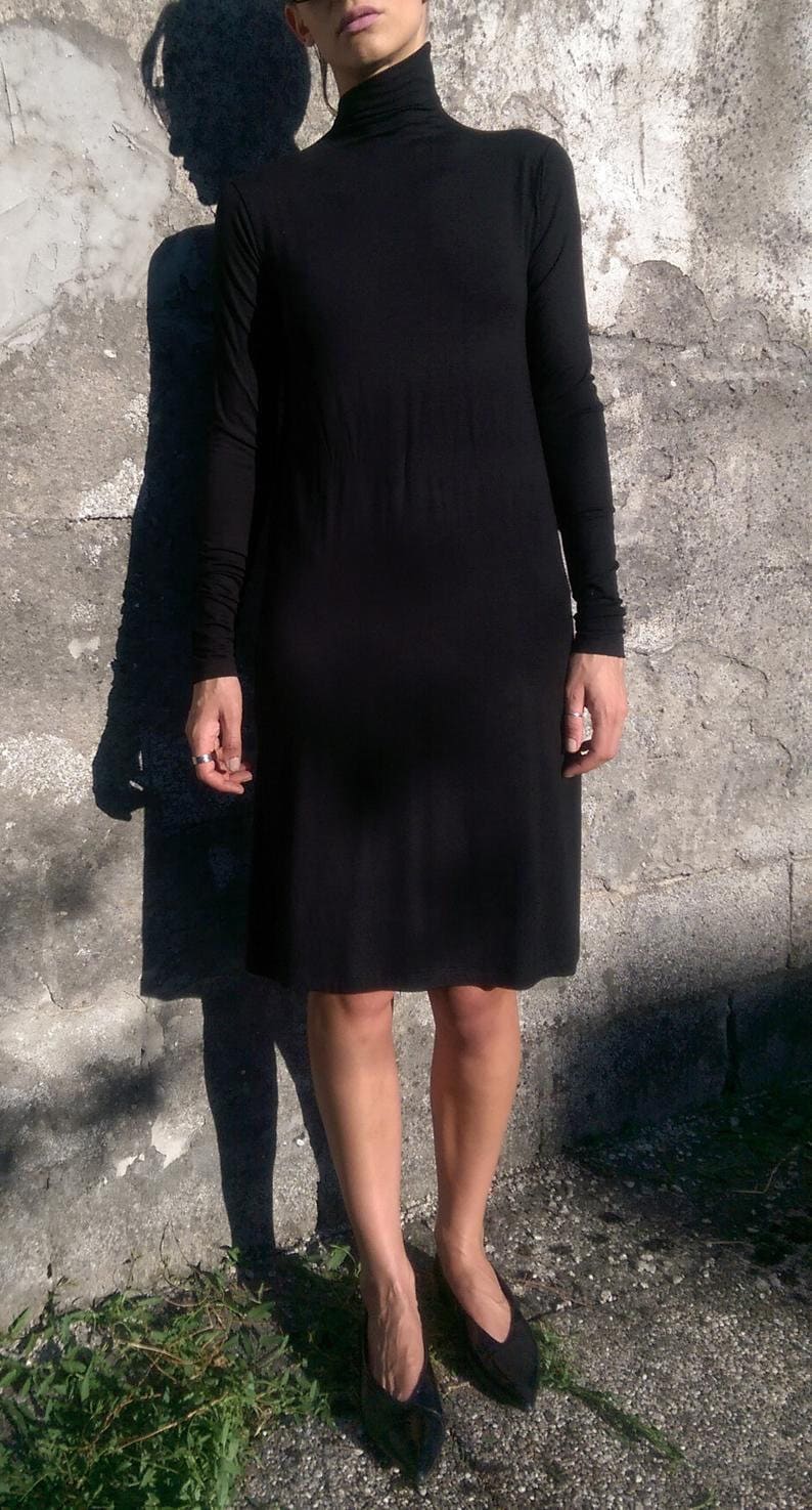 May include: A black turtleneck dress with long sleeves. The dress is fitted and falls to the knees. The model is wearing black shoes.