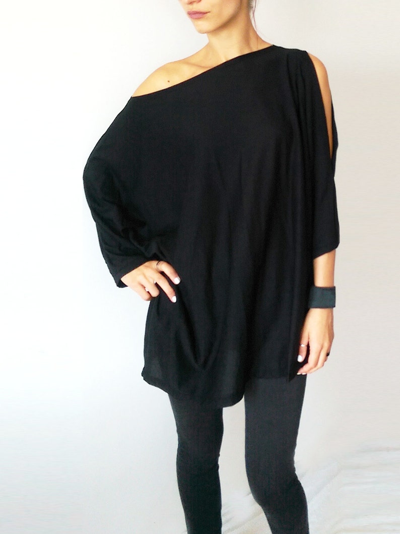 May include: A black, off-the-shoulder, long-sleeved top with a single cut-out on each shoulder. The top is loose-fitting and falls to the hips. The model is wearing black leggings.