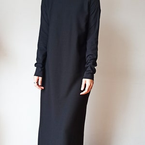 May include: A long, black turtleneck dress with long sleeves. The dress is floor-length and has a simple, elegant design. The person in the image is wearing black sunglasses and black shoes.