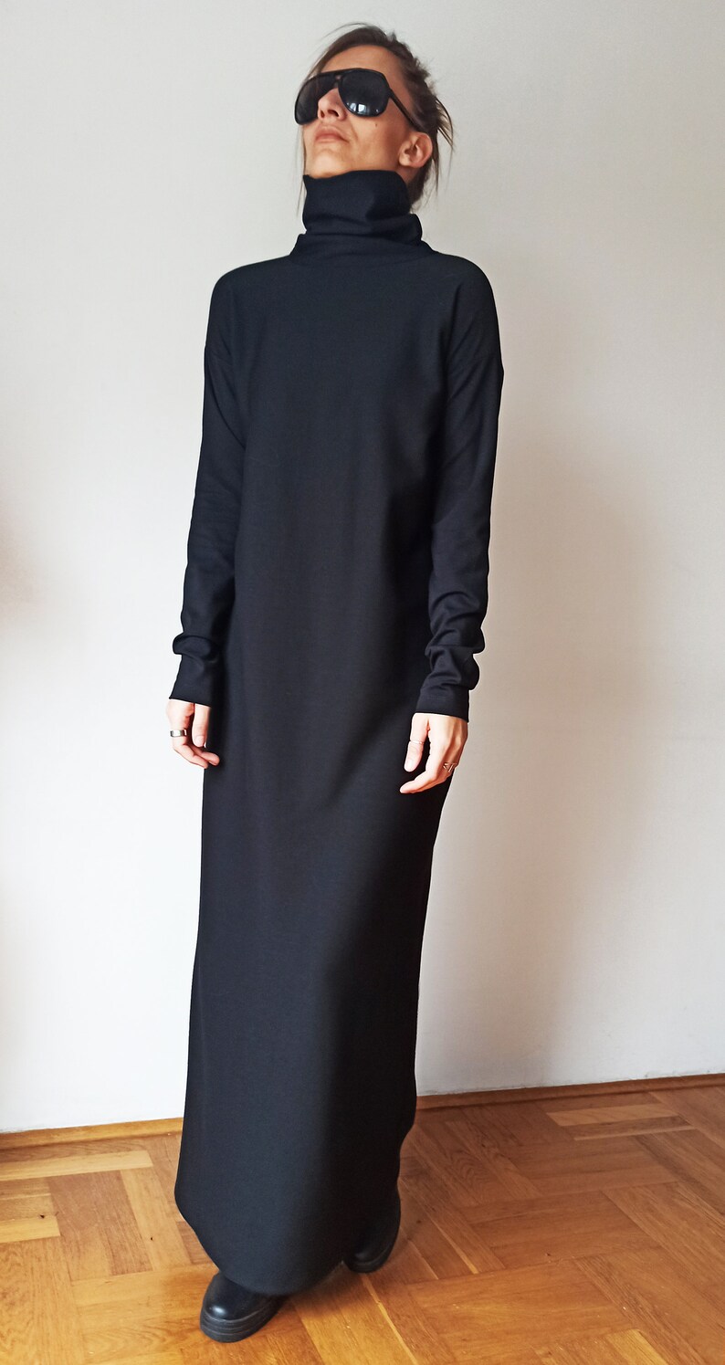 May include: A long, black turtleneck dress with long sleeves. The dress is floor-length and has a simple, elegant design. The person in the image is wearing black sunglasses and black shoes.