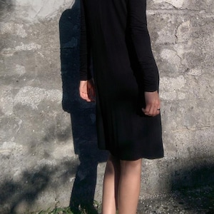 May include: A black mock neck dress with long sleeves. The dress is knee-length and has a fitted silhouette.
