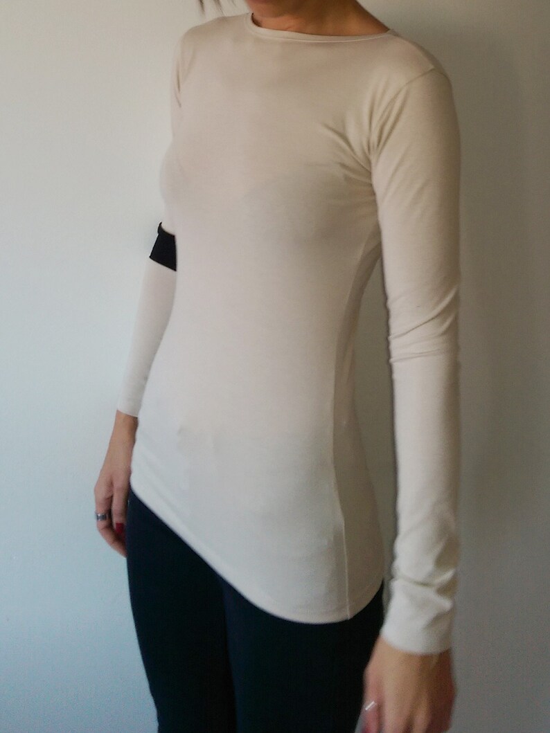 K&ouml;nnte beinhalten: Ein lang&auml;rmeliges, cremefarbenes Shirt mit figurbetonter Passform. Das Shirt hat einen runden Ausschnitt und ist aus einem weichen, dehnbaren Stoff gefertigt.