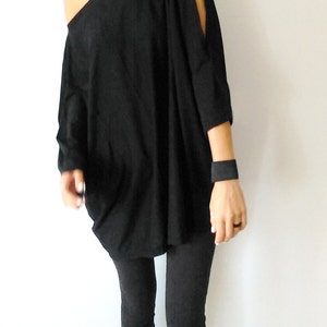 May include: A black off-the-shoulder top with long sleeves and cut-out shoulders. The top is loose-fitting and falls to the hips. The model is wearing black leggings.