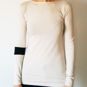 K&ouml;nnte beinhalten: Ein lang&auml;rmliges, cremefarbenes Shirt mit einem schwarzen Streifen am linken &Auml;rmel.