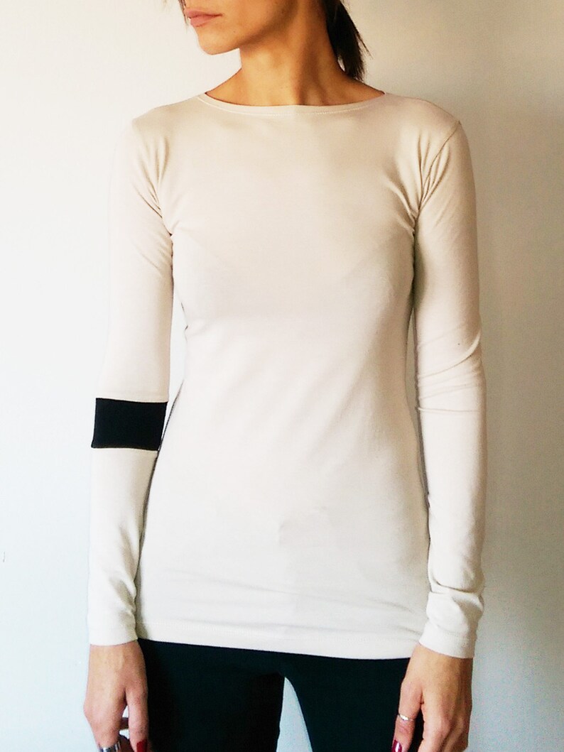 K&ouml;nnte beinhalten: Ein lang&auml;rmliges, cremefarbenes Shirt mit einem schwarzen Streifen am linken &Auml;rmel.