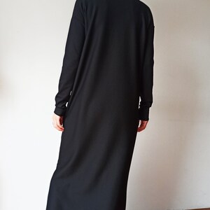 May include: A long, black dress with a high turtleneck collar and long sleeves. The dress is floor-length and appears to be made of a soft, flowing fabric. The person is wearing black shoes.