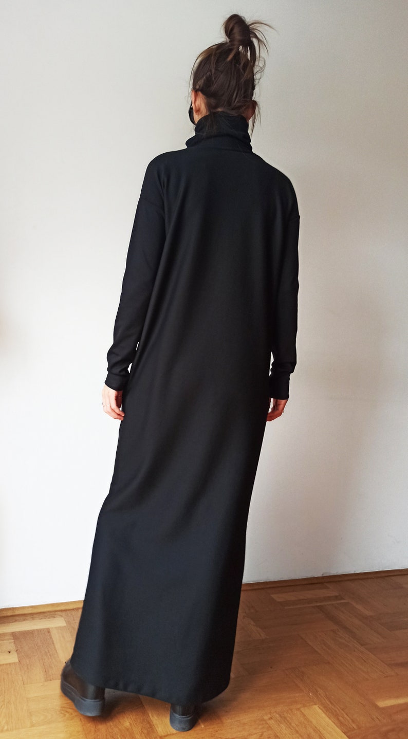 May include: A long, black dress with a high turtleneck collar and long sleeves. The dress is floor-length and appears to be made of a soft, flowing fabric. The person is wearing black shoes.