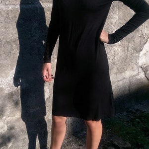 May include: A black turtleneck dress with long sleeves. The dress is fitted and falls to the knee. The model is wearing black pointed-toe shoes.