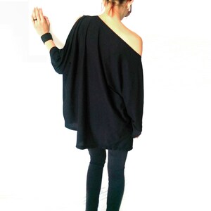 May include: A black off-the-shoulder top with long sleeves and a loose fit. The top is paired with black pants and black heels.
