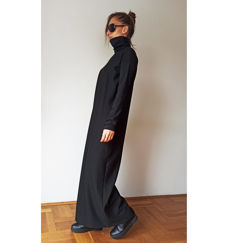 May include: A long, black turtleneck dress with long sleeves. The dress is floor-length and worn with black shoes. The person in the image is wearing sunglasses and has their hair up. The dress appears to be made of a soft, flowing fabric.