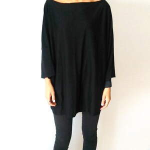 May include: A black, long-sleeved, oversized shirt with a boat neck. The shirt is worn with black leggings.