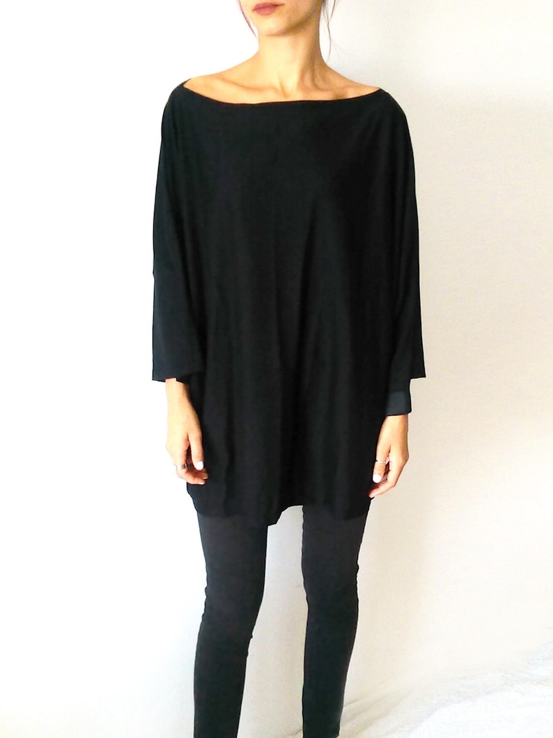 May include: A black, long-sleeved, oversized shirt with a boat neck. The shirt is worn with black leggings.