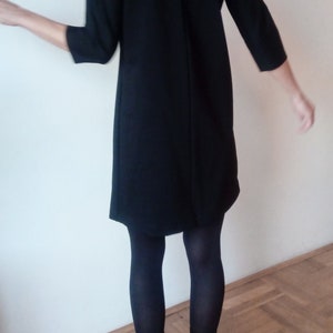 May include: A black dress with a long sleeve and a slightly flared skirt. The dress is worn with black tights and black heeled boots.