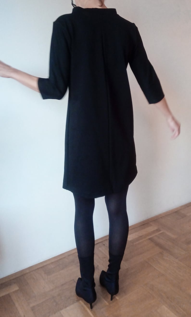 May include: A black dress with a long sleeve and a slightly flared skirt. The dress is worn with black tights and black heeled boots.