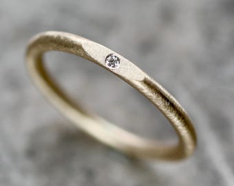 Puede incluir: Un anillo de banda de oro simple con un pequeño diamante engastado en el centro.