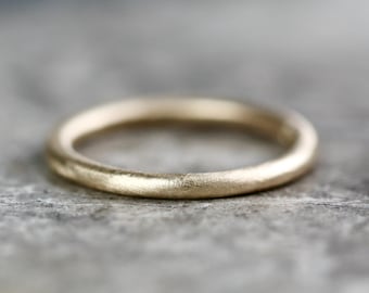 May include: A simple, brushed gold wedding band. The band is smooth and has a matte finish.