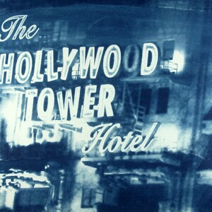 Può includere: Una fotografia vintage, in tonalità blu, dell'insegna dell'Hollywood Tower Hotel. L'insegna al neon, con le parole "The Hollywood Tower Hotel", è illuminata su uno sfondo scuro, suggerendo una scena notturna. L'immagine ha un'estetica retrò classica.