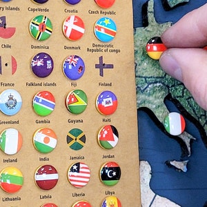 May include: A close-up of a wooden board with small round buttons featuring flags of different countries. The buttons are arranged in rows and columns, with each button labeled with the name of the country it represents. The board is set against a green and blue background, which appears to be a map of the world.
