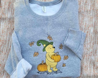 May include: Gray sweatshirt with a Winnie the Pooh character wearing a witch hat and holding a pumpkin. The character is surrounded by fall leaves.