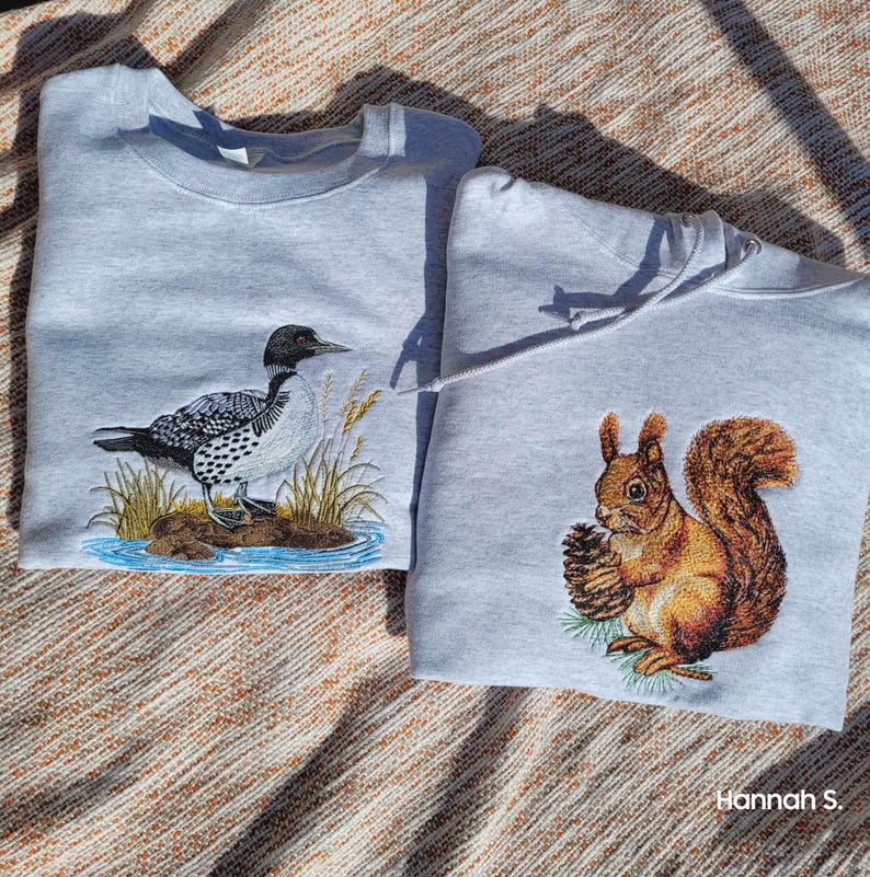 Pu&ograve; includere: Due felpe grigie con disegni ricamati. Una felpa presenta un uccello tuffatore su un lago, l'altra presenta uno scoiattolo che tiene una noce. Entrambe le felpe hanno una vestibilit&agrave; comoda.