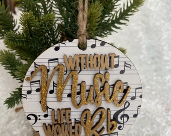 May include: A round wooden ornament with a white background and black musical notes. The ornament has gold glitter lettering that reads "Without Music Life Would Be".